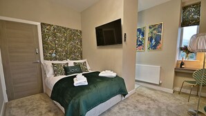A bedroom with a bed, a TV mounted on the wall, and artwork on the walls. - The Milan Suite at Moat House (Lancashire)