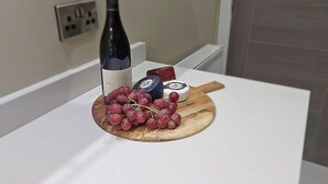 A white countertop with a wooden cutting board holding a bottle of wine, a small cheese wheel, and a bunch of grapes. - The Milan Suite at Moat House (Lancashire)