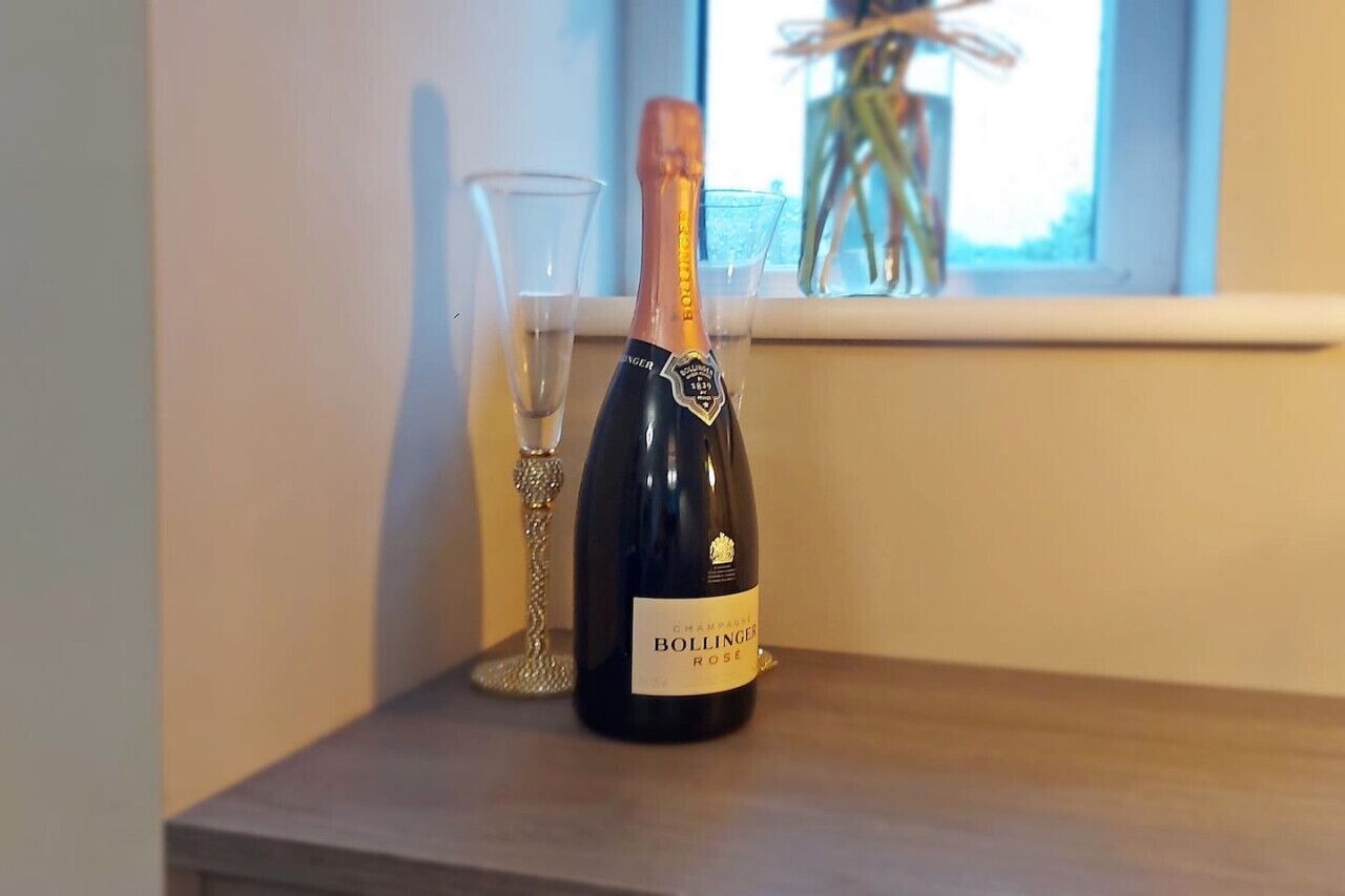 Een fles Bollinger Rosé Champagne op een houten oppervlak, naast een glas.