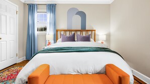 A neatly arranged bedroom with a large bed, two bedside tables, a window with curtains, and a wall-mounted artwork. - 5bd Vibrant Haven: Basketball - 10mins to Airport (Charlotte)