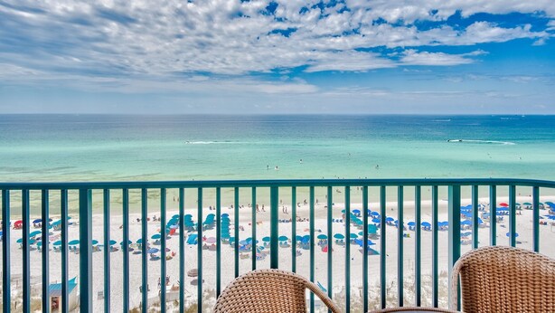 A balcony with a view of a beach with umbrellas and people. - Sunset Views, Gulf Front at Jade East Towers (Destin)