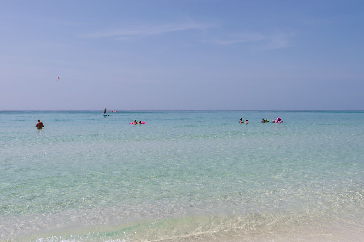 Una platja amb aigua turquesa cristal·lina, persones nedant i fent paddle surf.