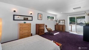 A bedroom with a bed, two wooden dressers, a chair, a desk, and a large window with a view of a vehicle outside. - Cozy home on private acreage,
 with a short walk to downtown Leavenworth. (Leavenworth)