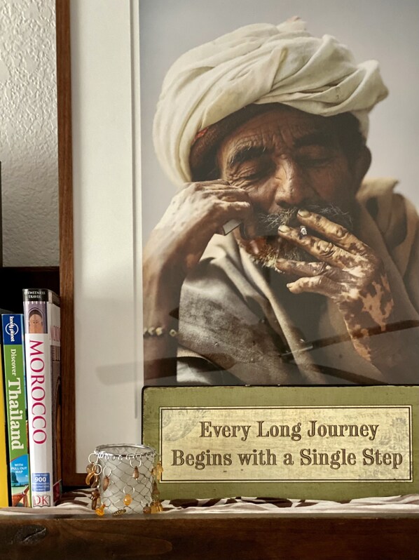 Fotografia emoldurada de uma pessoa com turbante, rodeada por livros de viagem e uma placa com uma frase motivacional.