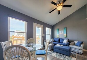 A spacious living room with a glass dining table, blue upholstered sofa, and a ceiling fan. - Seashell Cove: Waterfront Bliss at Bermuda Landing (North Topsail Beach)