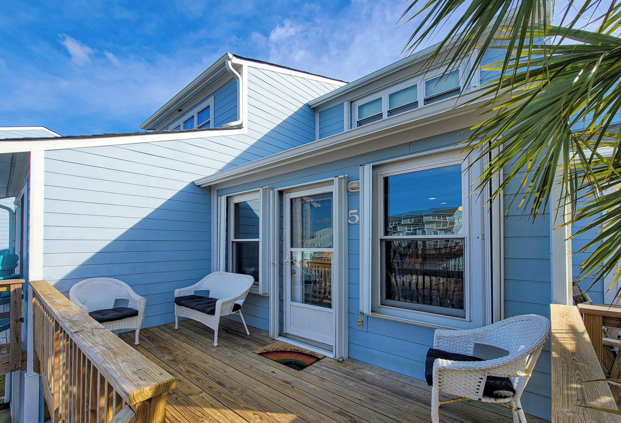 A coastal house with a deck, two wicker chairs, and a wooden railing.