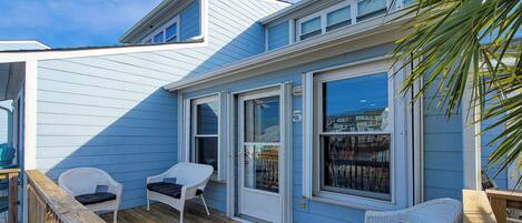 A coastal house with a deck, two wicker chairs, and a wooden railing.