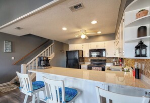 A modern kitchen with white cabinetry, a central island with bar stools, a ceiling fan, and a stone backsplash. - Seashell Cove: Waterfront Bliss at Bermuda Landing (North Topsail Beach)