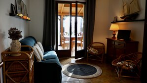 Un accogliente soggiorno con divano, poltrone, una lampada e vista su uno spazio esterno attraverso una porta vetrata.
