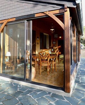 Un espace repas comprenant une grande table et des chaises, une porte-fenêtre et un sol carrelé en pierre.