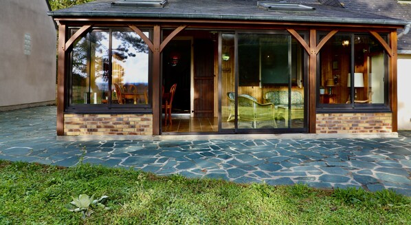 Un patio couvert doté d’un sol en pierre et de portes vitrées donnant sur un espace intérieur aménagé avec des meubles en osier.