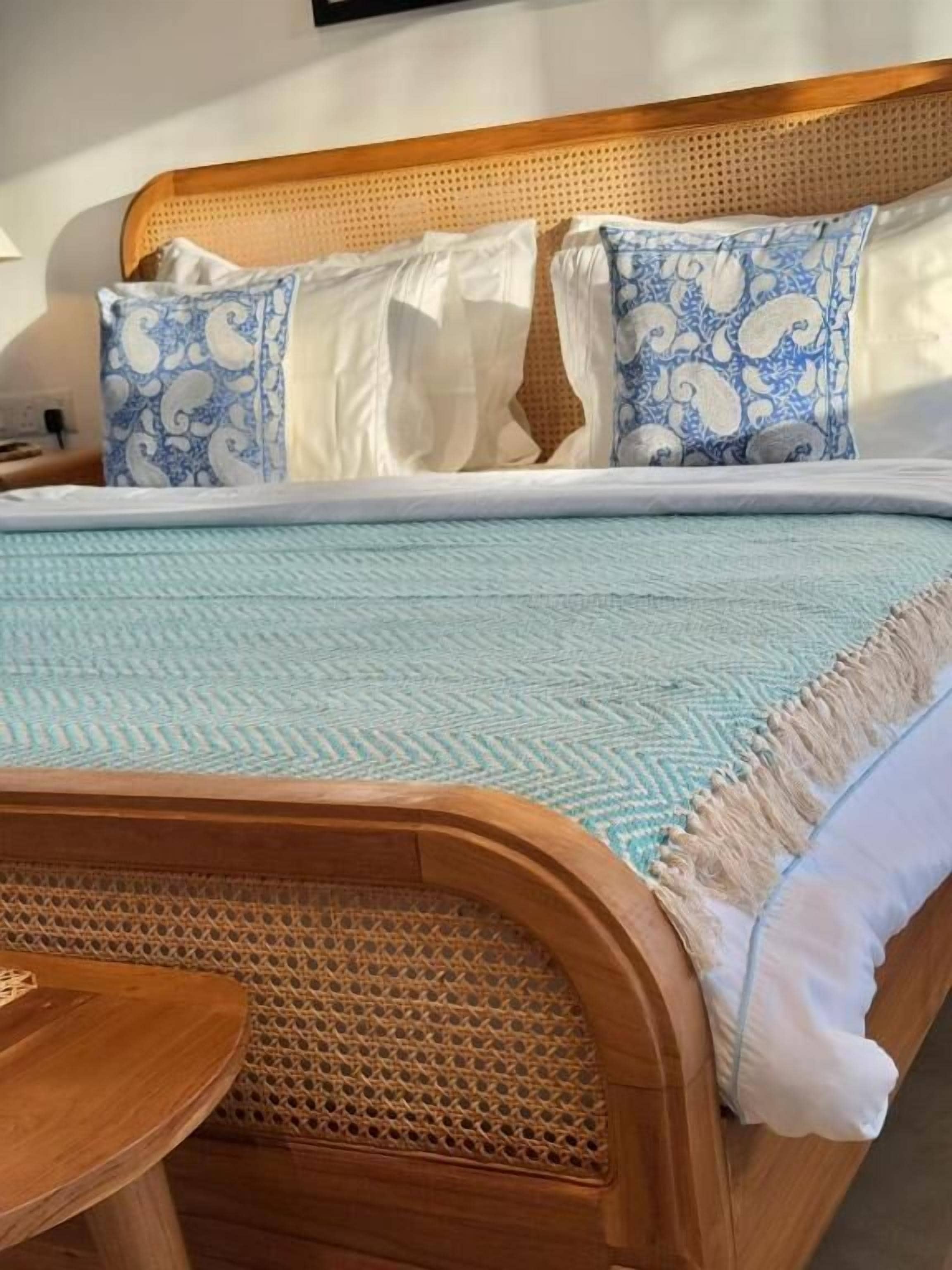 A bed with a wooden headboard, white and blue patterned pillows, and a light blue bedspread.