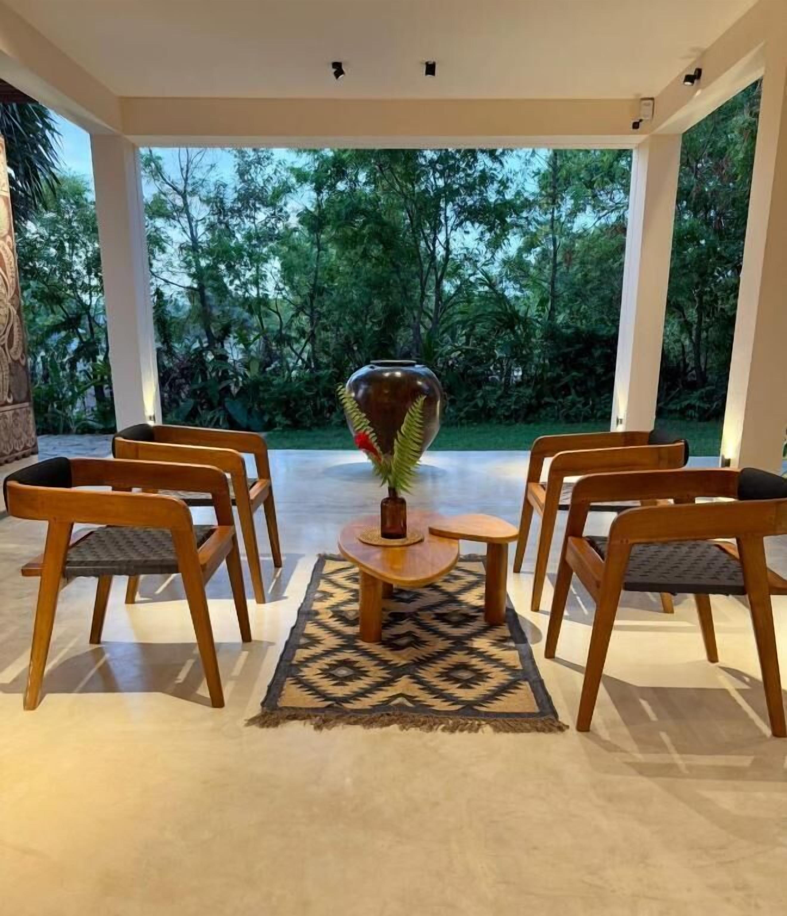 Un área de estar exterior moderna con sillas de madera y una mesa central, rodeada por un tapete estampado.
