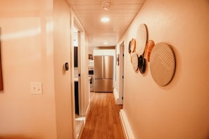 A narrow hallway with wooden flooring, a stainless steel refrigerator, and wall-mounted decorative plates.