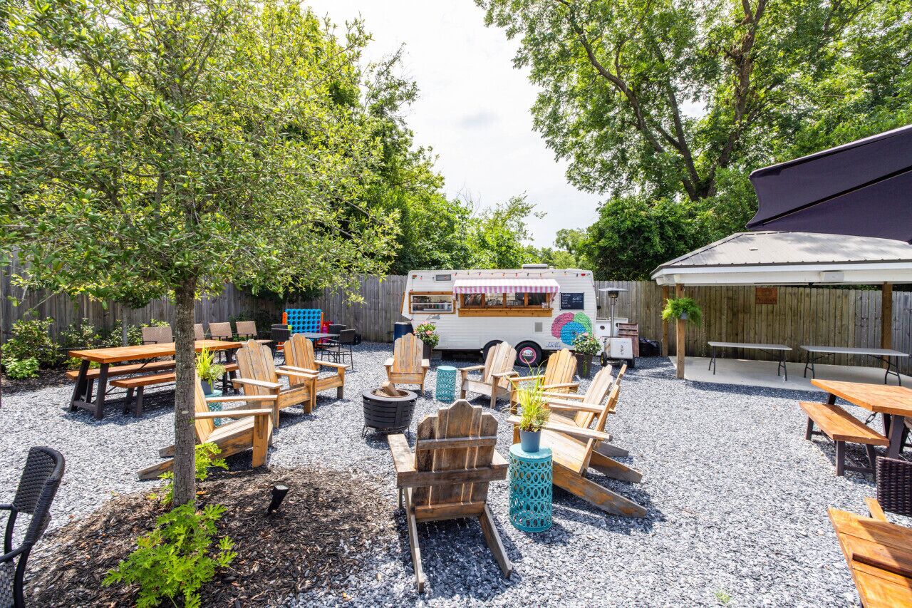 An outdoor seating area with wooden tables and chairs, a food truck, and a covered patio.