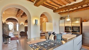 Une cuisine moderne dotée d’un îlot central, d’appareils électroménagers en acier inoxydable et de poutres apparentes en bois.