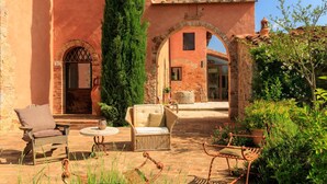 Une cour avec des sièges en plein air, un grand arbre et un bâtiment doté d’arcades et d’un toit en tuiles.