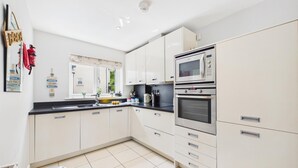 A modern kitchen with white cabinets, a black countertop, and stainless steel appliances including a microwave and oven. - The Beachhouse - 2 Bed Townhouse - Saundersfoot (Saundersfoot)