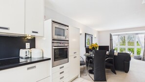 A modern kitchen with a built-in oven, a microwave, and a toaster. There is a dining area with a table and chairs.