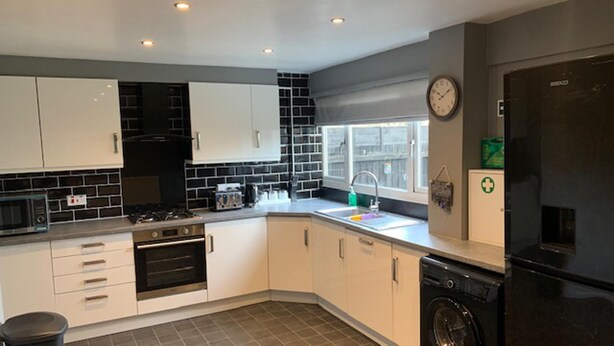A modern kitchen with white cabinets, a black microwave, a stove, a sink, and a black washing machine.