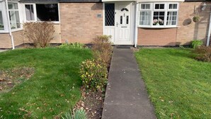 A residential building with a front door, a small garden, and a pathway leading to the entrance.