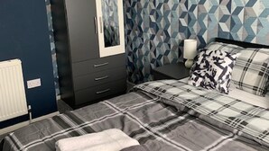 A bedroom with a bed, a wardrobe, a nightstand, and a geometric-patterned wall.