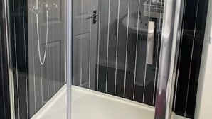 A glass-enclosed shower stall with a white floor, a handheld showerhead, and a wall-mounted faucet.