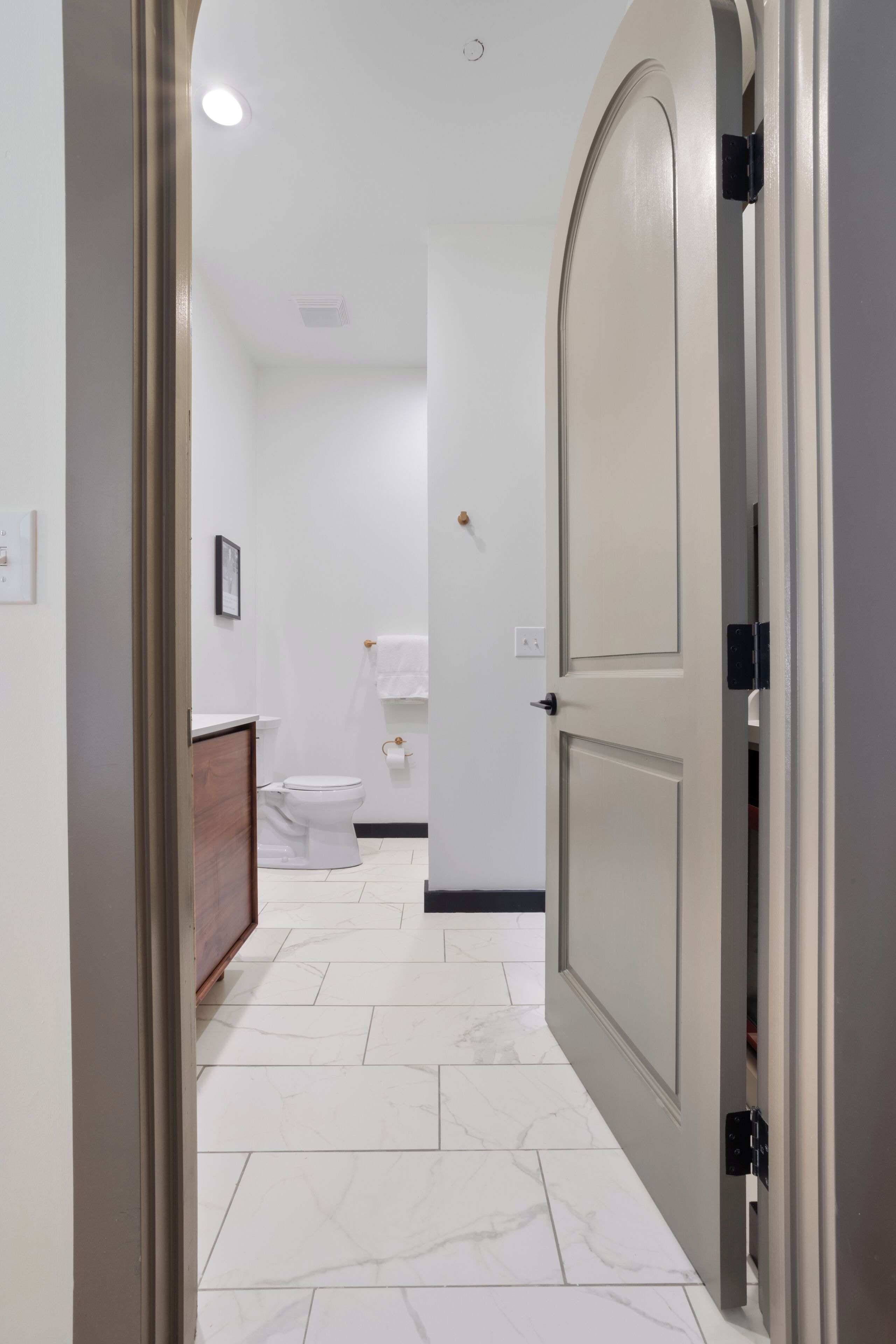 A hallway with a white tiled floor, a closed door on the right, and a toilet visible in the background.