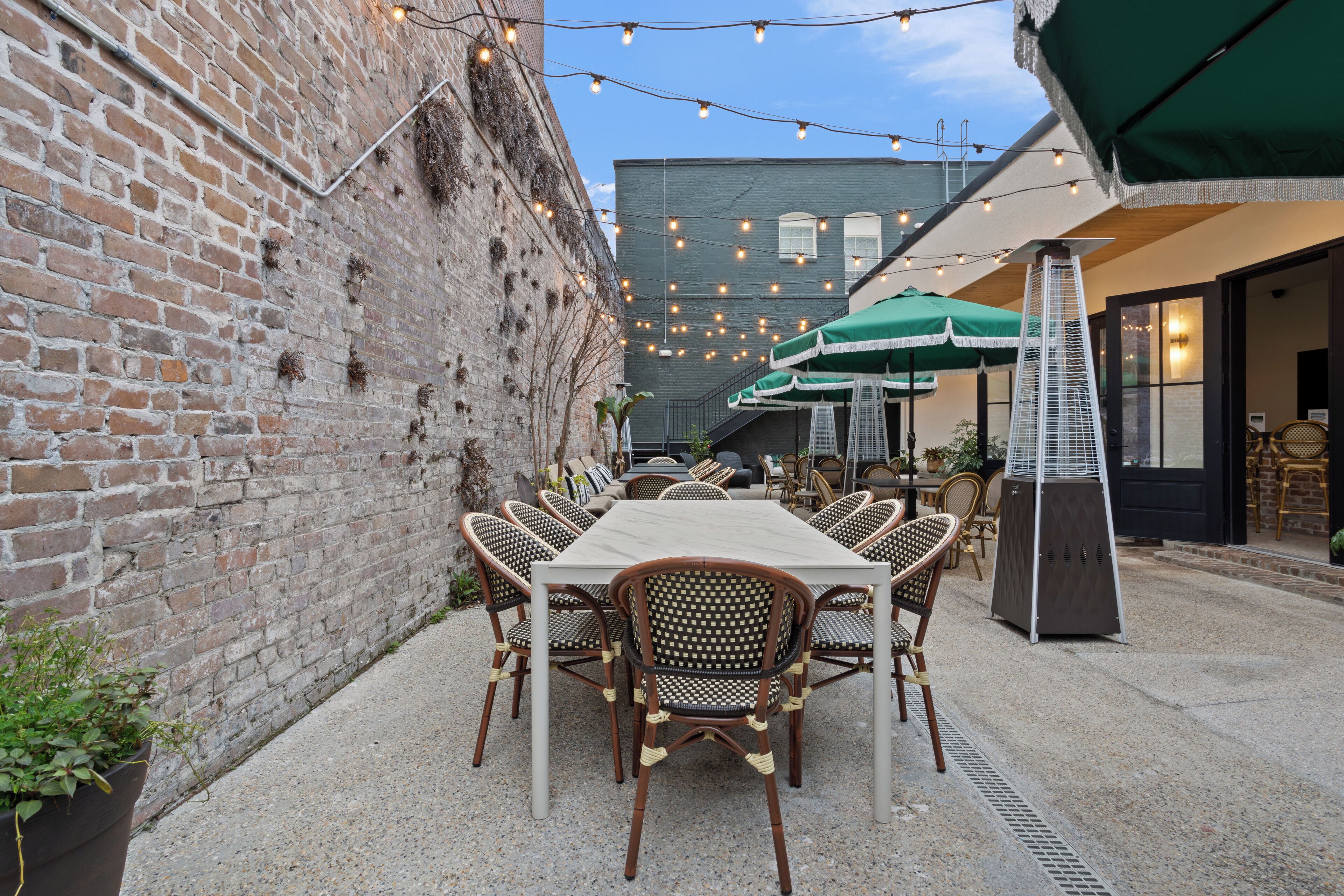 An outdoor dining area with a brick wall, string lights, and a table with chairs.