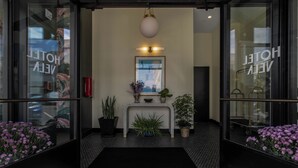 A hotel entrance with a reception desk, potted plants, and a black mat. - Hotel Vela (Gulfport)