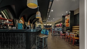 A modern bar area with a black counter, metal stools, and hanging wicker lamps. - Hotel Vela (Gulfport)