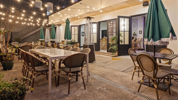 An outdoor dining area with wicker chairs and tables, string lights, and umbrellas. - Hotel Vela (Gulfport)