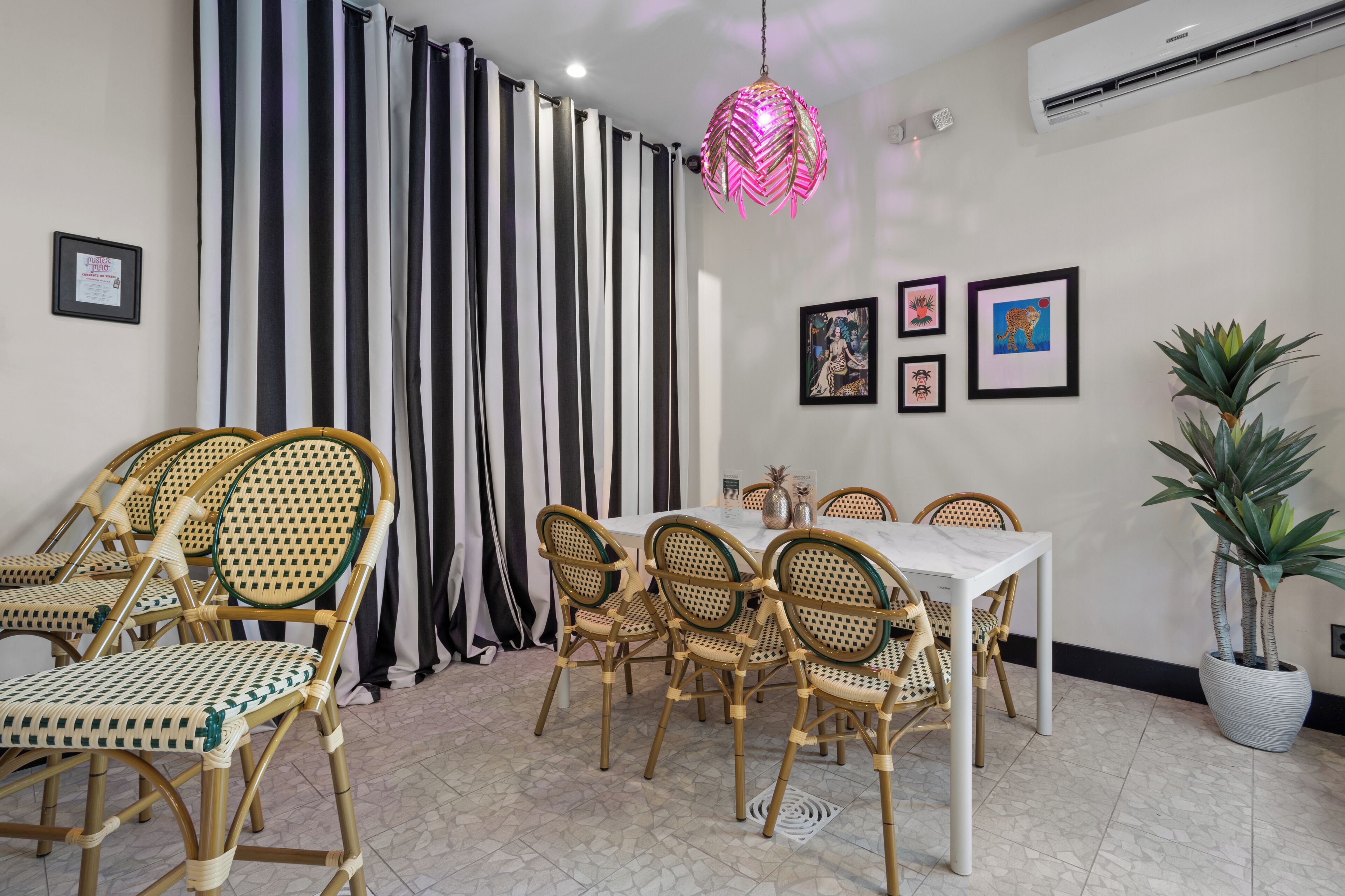 A dining area with a white table and chairs, striped curtains, and a potted plant.