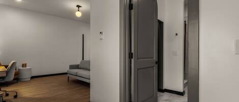 A modern interior with a wooden floor, a grey sofa, a desk with a chair, and a closed door.