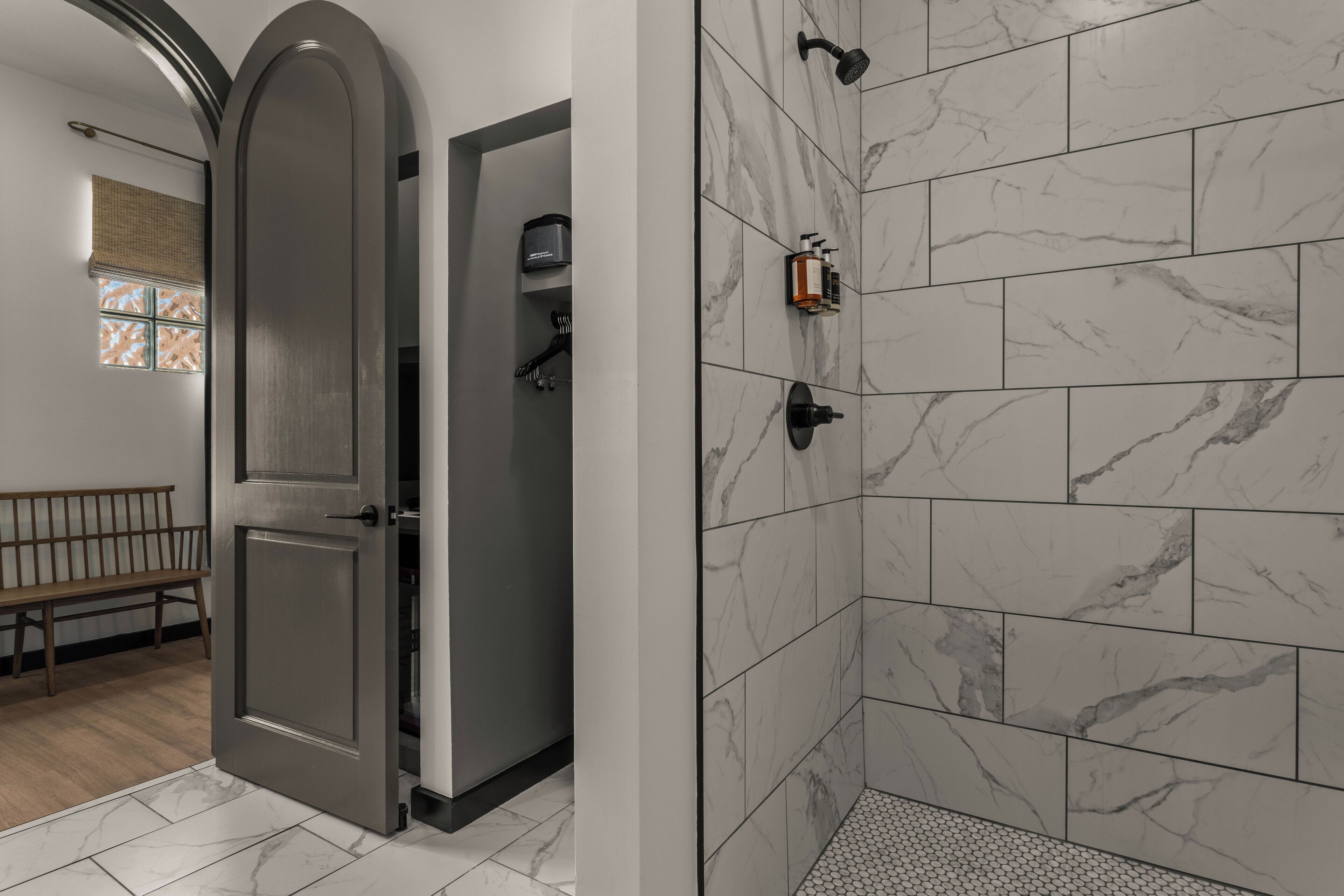 A modern bathroom with a shower area, a bench, and a door leading to a room.