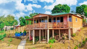 Une maison en bois dotée d’un balcon, entourée de verdure et sous un ciel dégagé.