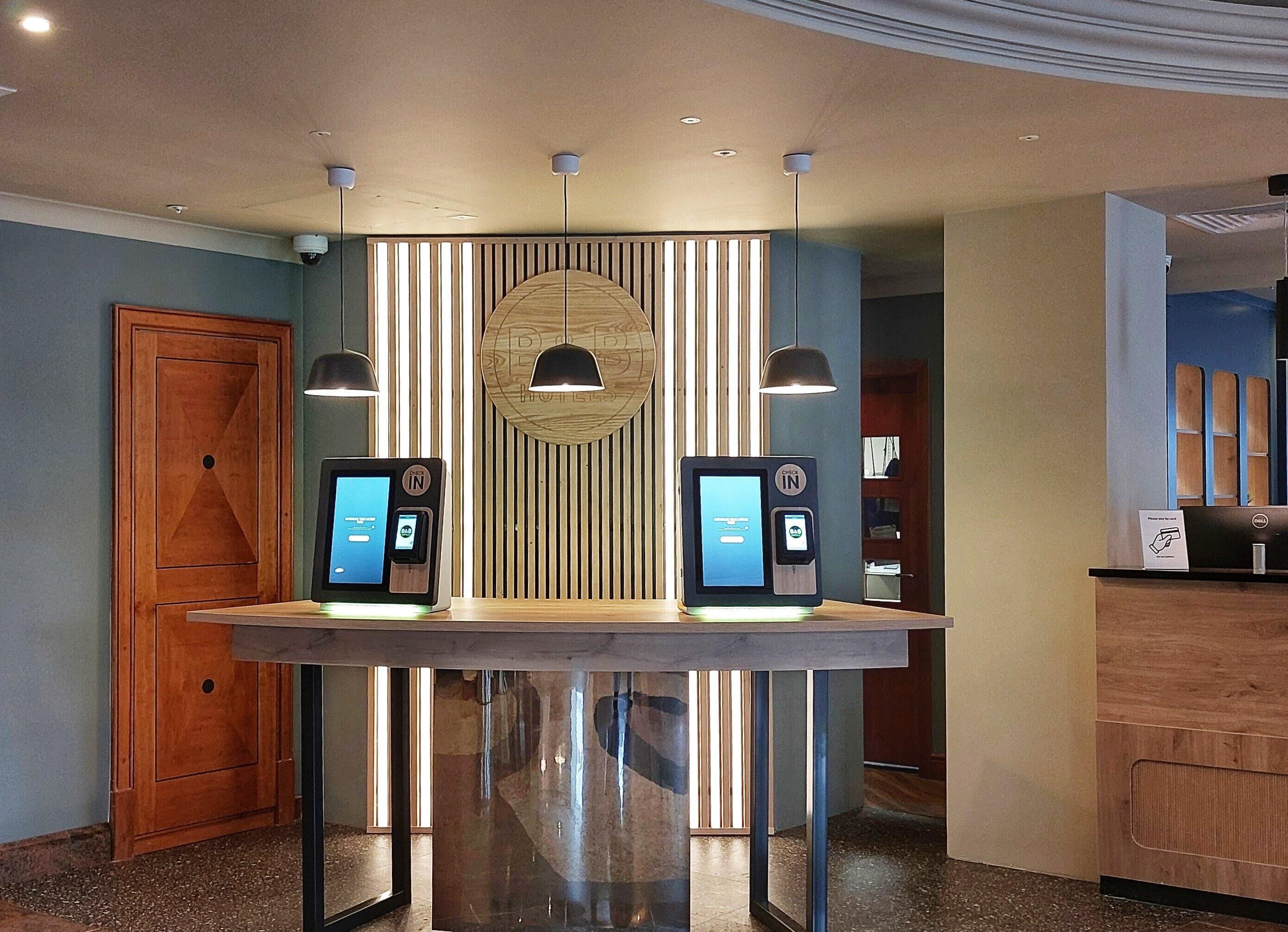 A reception area with two self-service kiosks, a wooden door, and a modern ceiling design.