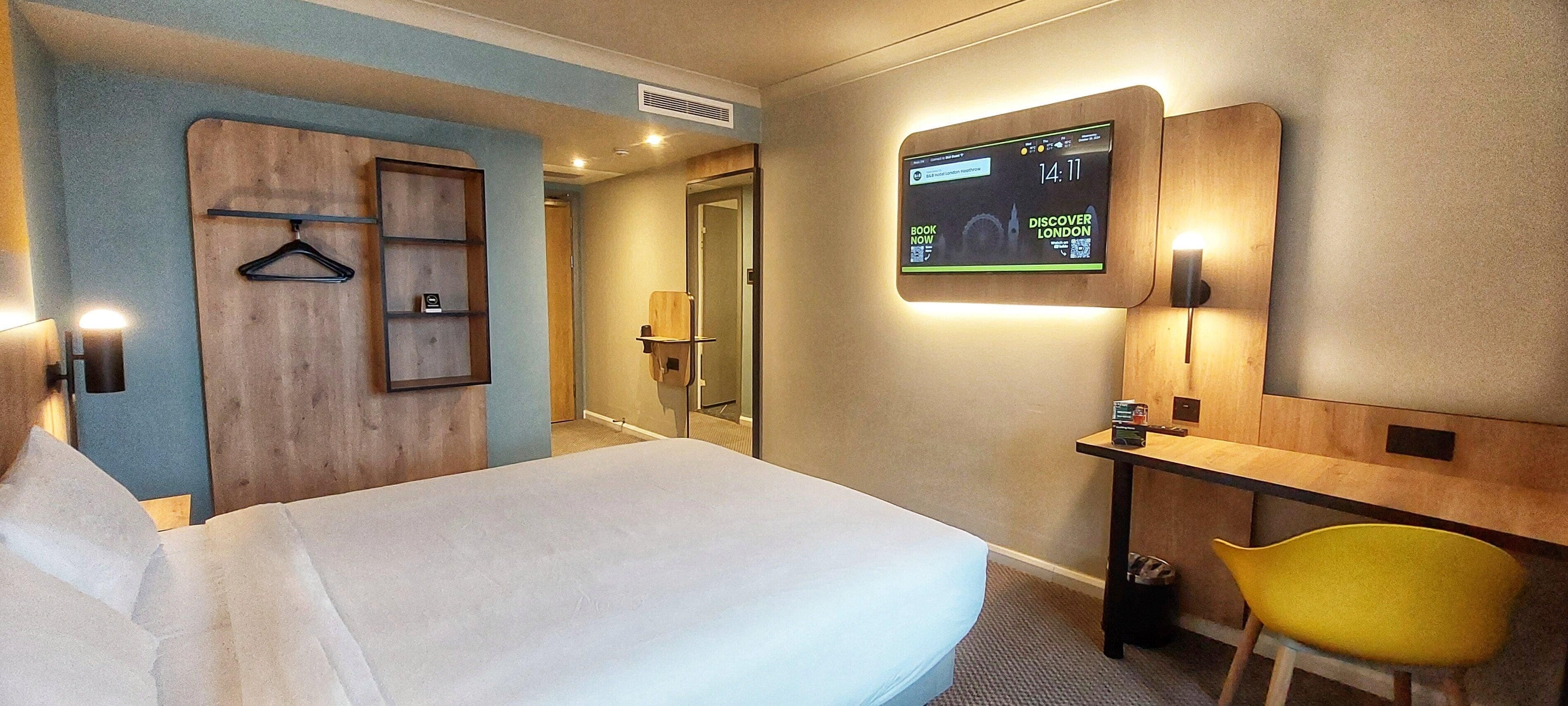 Ein Hotelzimmer mit einem Bett, einem Schreibtisch, einem Sessel, einem an der Wand befestigten Fernseher und einem Holzschrank.