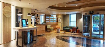 Un moderno vestíbulo de hotel con un mostrador de recepción, una zona de estar y un puerta de cristal que da al exterior.
