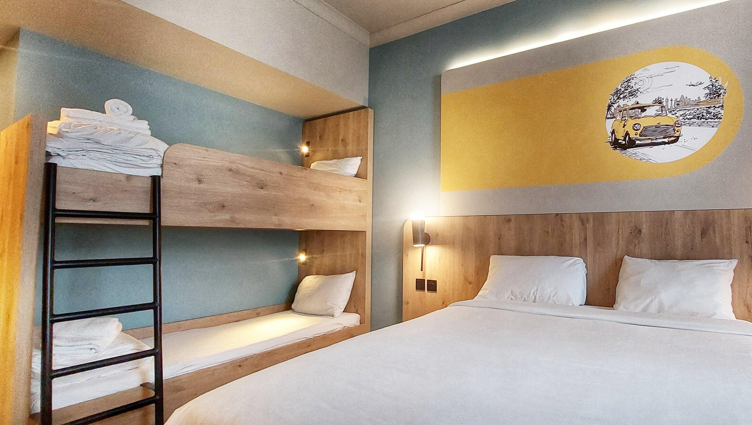 A bunk bed room with a wooden ladder, a single bed with white bedding, and a wall-mounted light fixture.