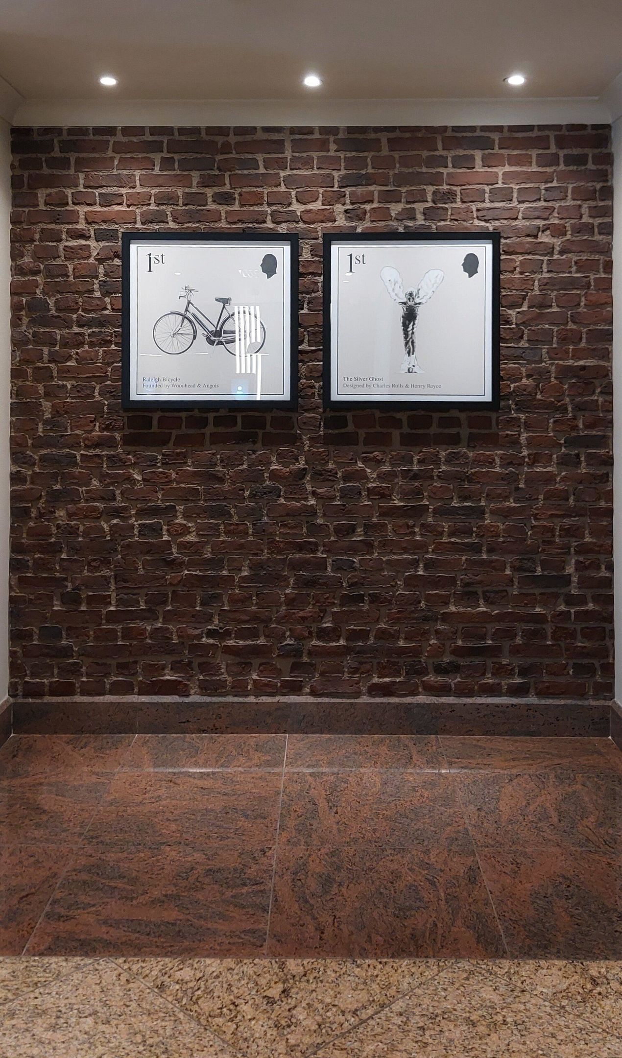 Deux œuvres d’art encadrées sont accrochées à un mur de briques : l’une représente un vélo, l’autre une figure ailée.