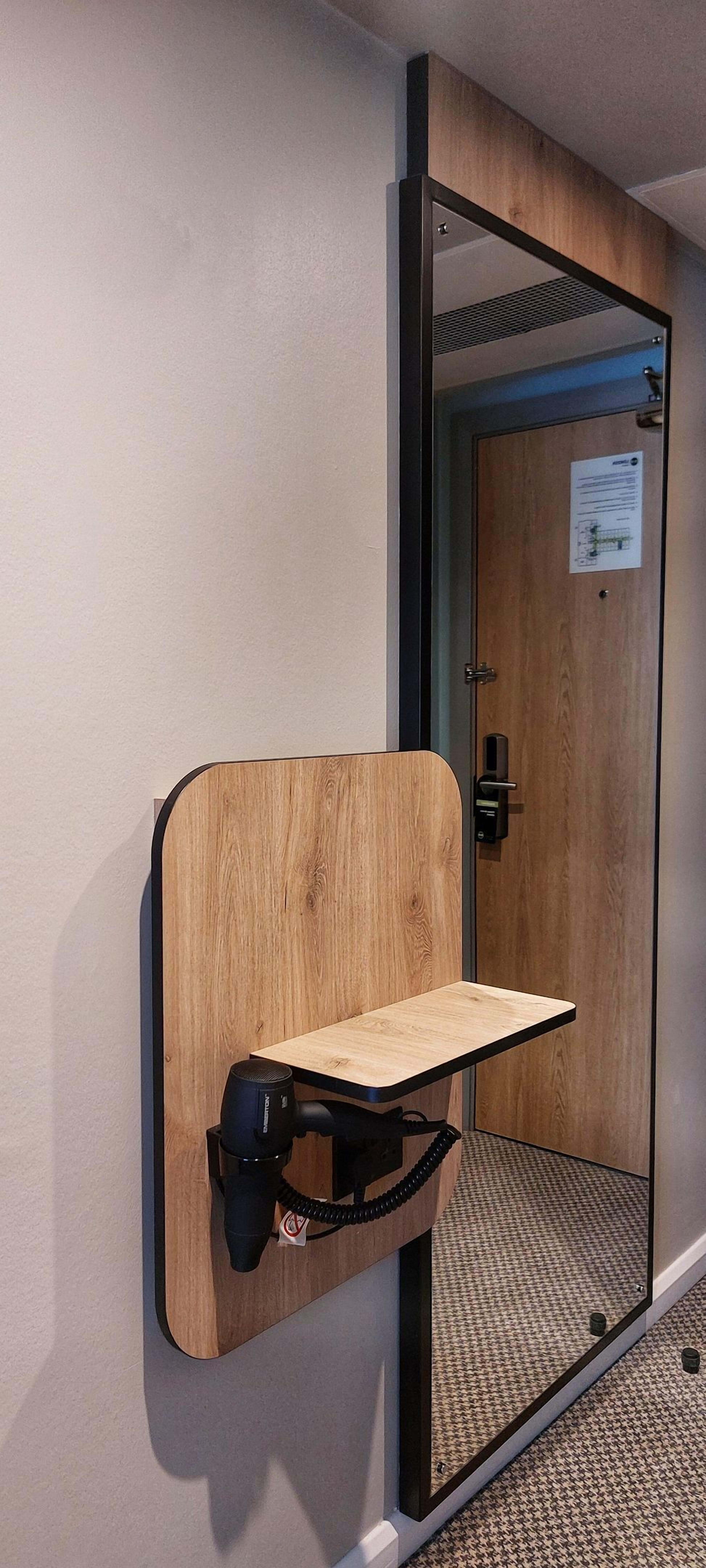 Un espejo con marco de madera, un estante, una puerta con cerradura y suelo alfombrado.