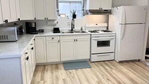 A modern kitchen with white cabinets, a microwave, a sink, a stove, and a refrigerator.