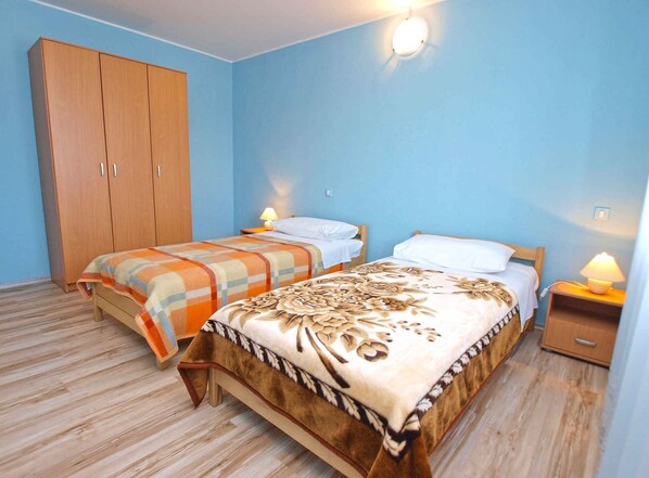 A bedroom with two beds, wooden wardrobe, and bedside lamps.