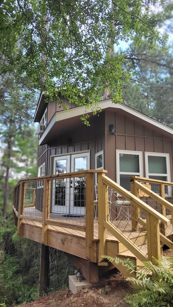 A wooden deck with a staircase leading to a house with large windows and a balcony.