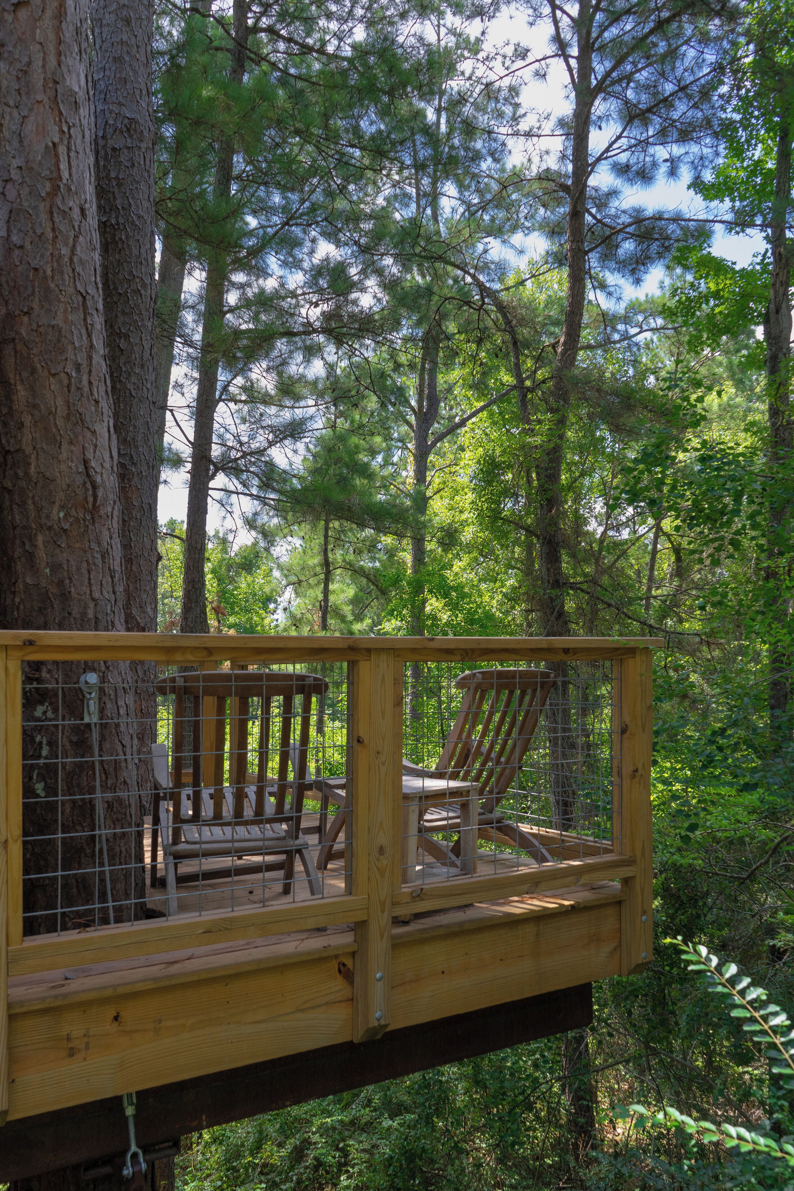 Une terrasse en bois avec deux chaises et une table, entourée d’arbres.