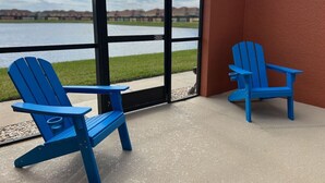 Two blue Adirondack chairs on a concrete patio with a view of a lake and buildings in the background. - 4BR Townhome 6 mile to Disney (Kissimmee)