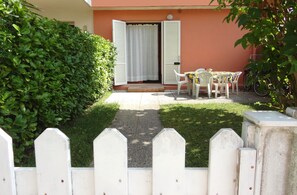 Un patio con mesa y sillas, cerca viva y valla de piquetes blancos.