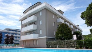 Ein modernes mehrgeschossiges Gebäude mit Balkonen, einem Schwimmbad und einer Hecke.