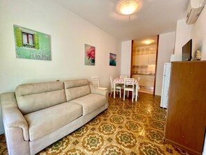 Una sala de estar con un sofá color beige, una mesa de comedor con sillas y una cocina al fondo.